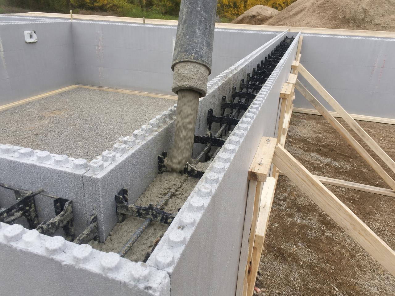 Concreto sendo lançado por mangote no interior das formas isolantes do sistema ICF, com armaduras e travas plásticas visíveis na cavidade